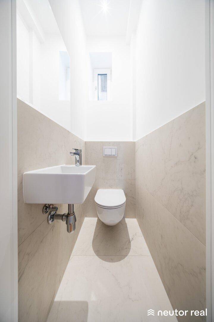 Modernes Gäste-WC mit Wand-WC, kleinem Waschbecken und hellen Fliesen.