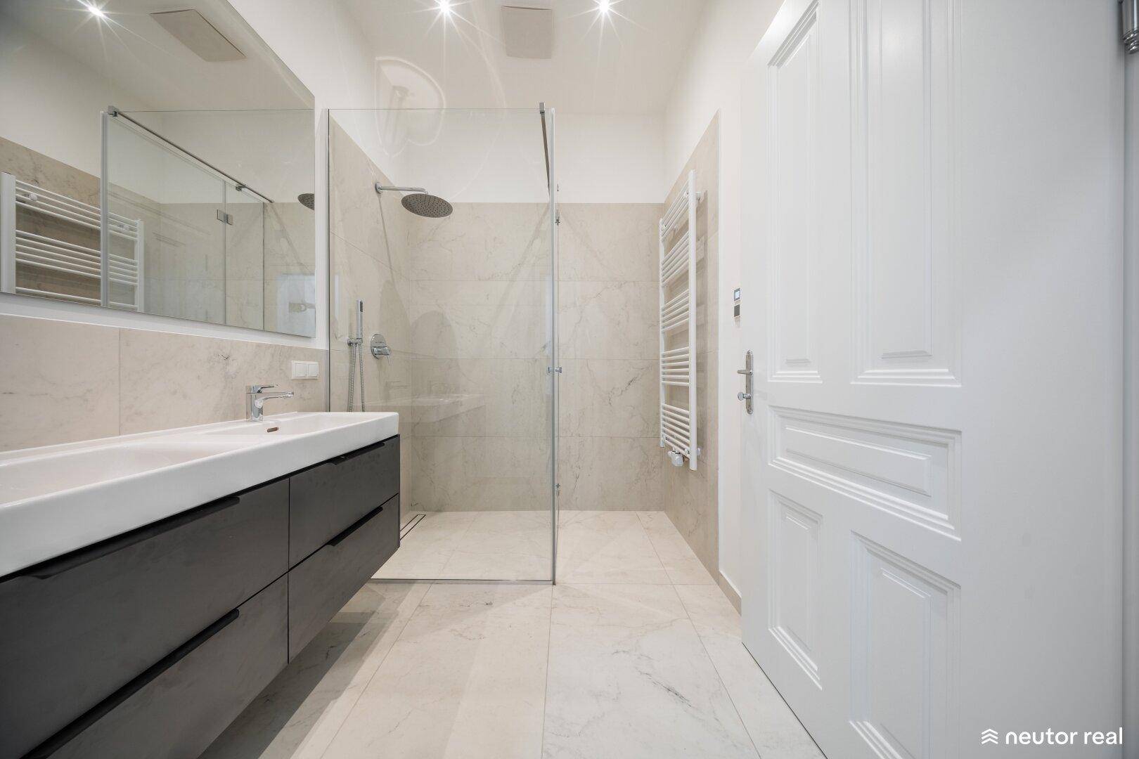 Modernes Badezimmer mit Doppelwaschbecken, begehbarer Dusche und beheiztem Handtuchhalter.