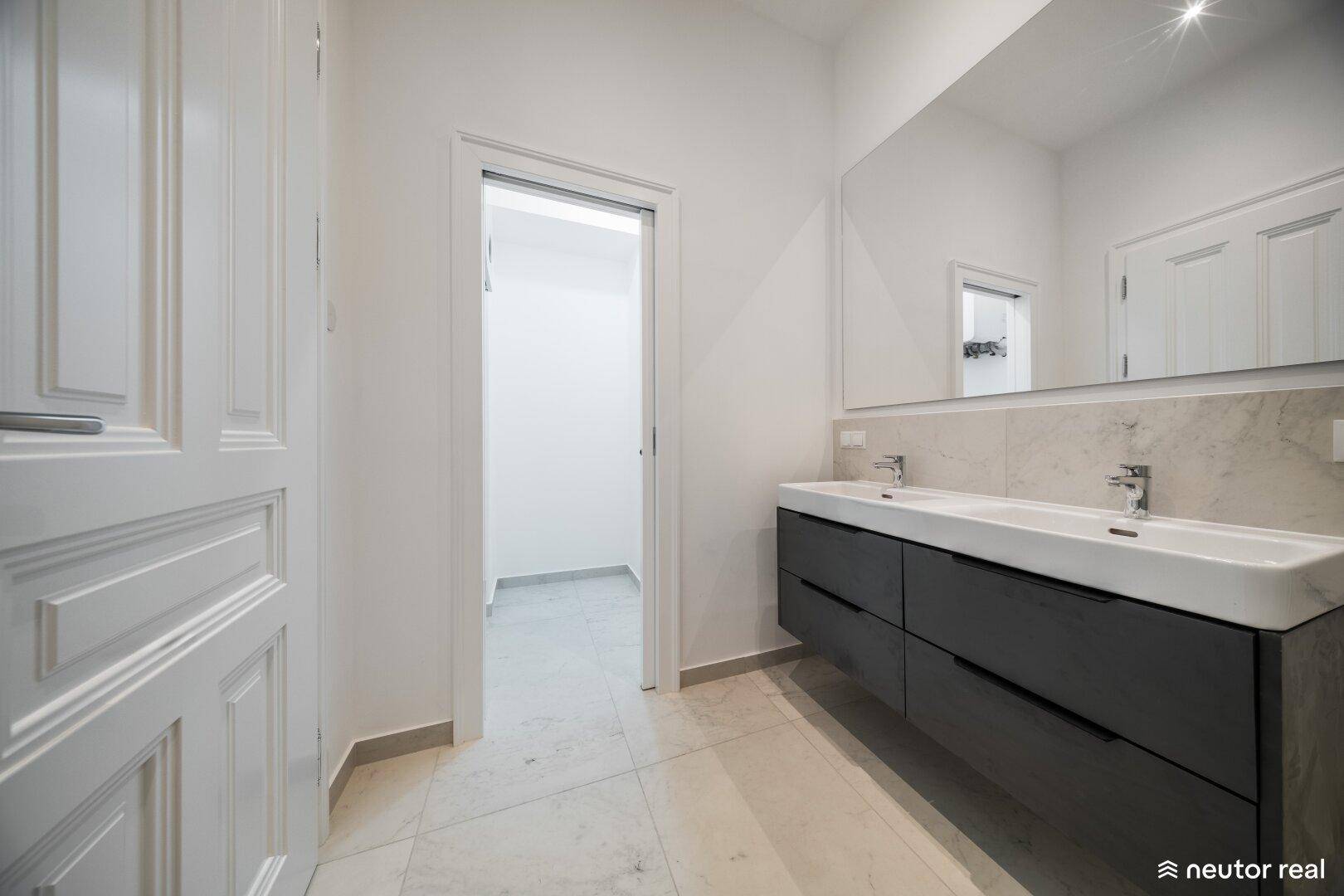 Modernes Badezimmer mit Doppelwaschbecken und Zugang zu einem weiteren Raum, möglicherweise einem Gäste-WC.