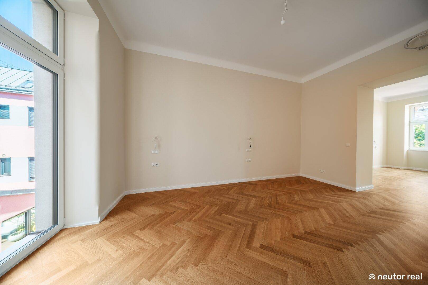 Großzügiges Wohnzimmer mit Fischgrätparkett und bodentiefen Fenstern, die viel Licht hereinlassen.