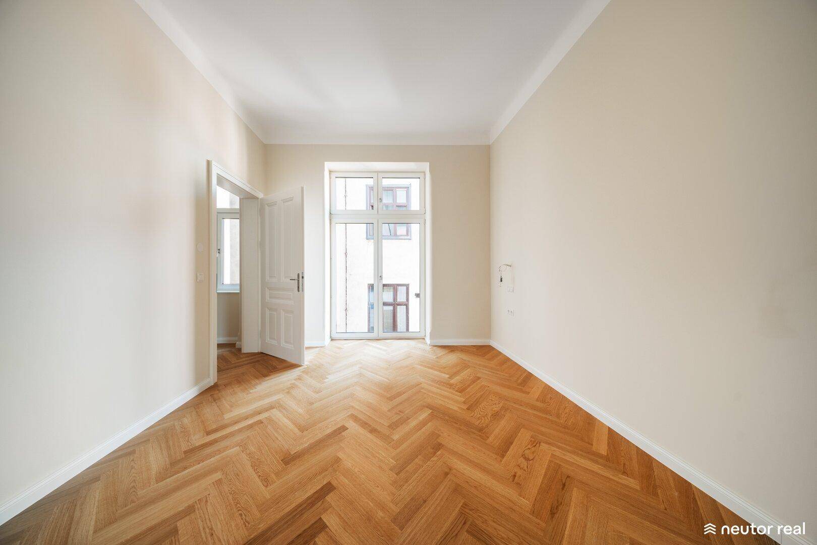 Heller Wohnraum mit Fischgrätparkett und Zugang zu einem französischen Balkon, der viel Licht spendet.