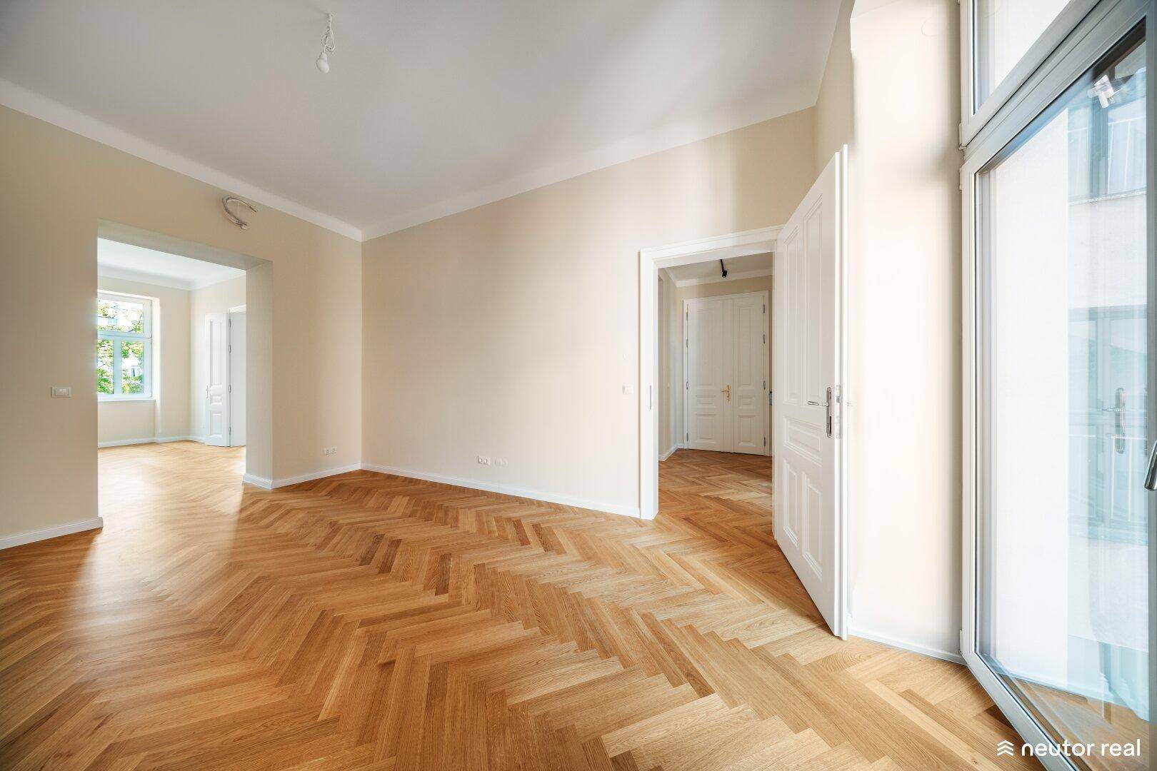 Helles Wohnzimmer mit Fischgrätparkett und Zugang zu weiteren Räumen, ideal für offenes Wohnen.