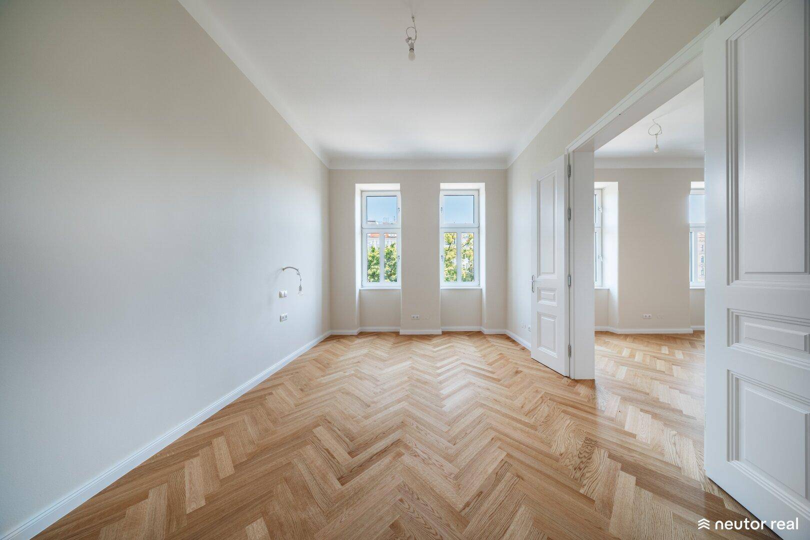 Geräumiges Wohnzimmer mit klassischem Fischgrätparkett und hohen Decken, bereit zur individuellen Gestaltung.