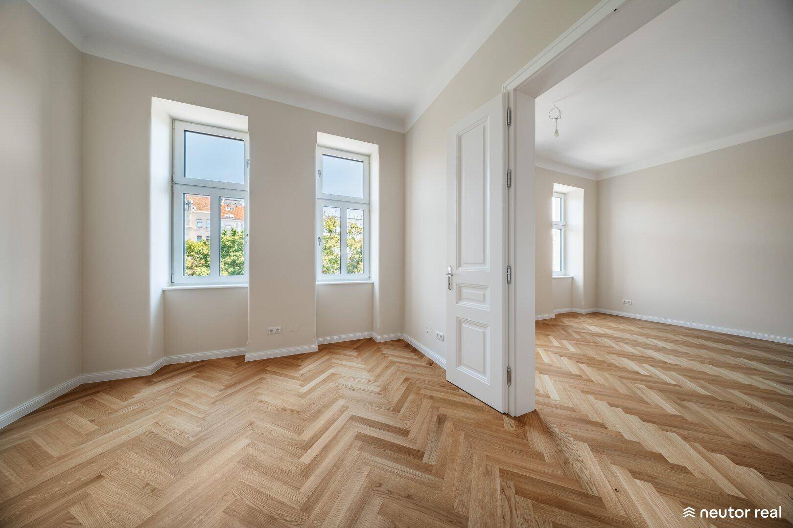 Helles Wohnzimmer mit Fischgrätparkett und zwei großen Fenstern, die den Raum mit Licht füllen.