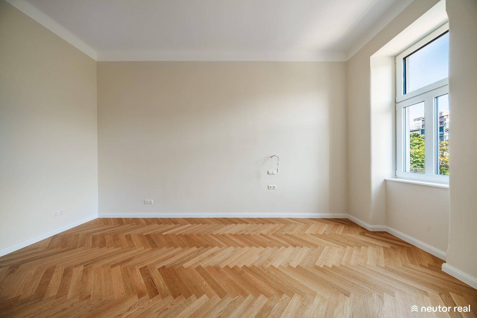 Helles Wohnzimmer mit Fischgrätparkett und einem großen Fenster, das den Raum mit Tageslicht durchflutet.