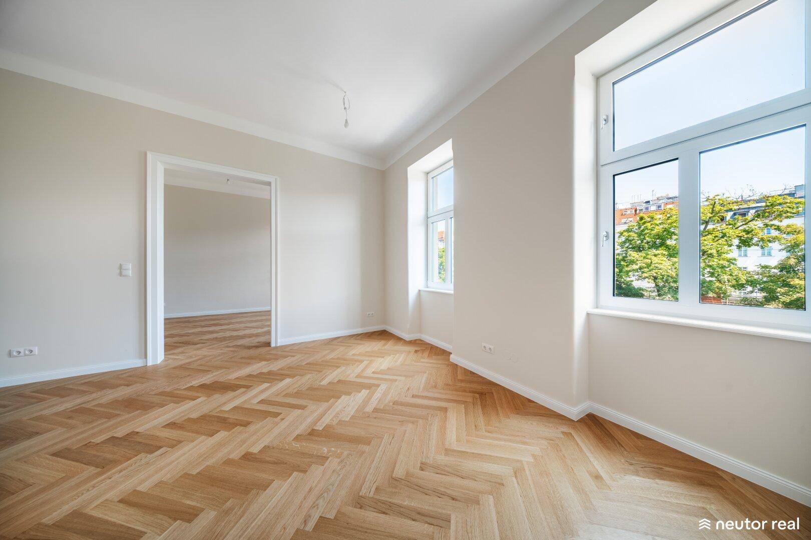 Helles Wohnzimmer mit Fischgrätparkett und großen Fenstern mit Blick ins Grüne.