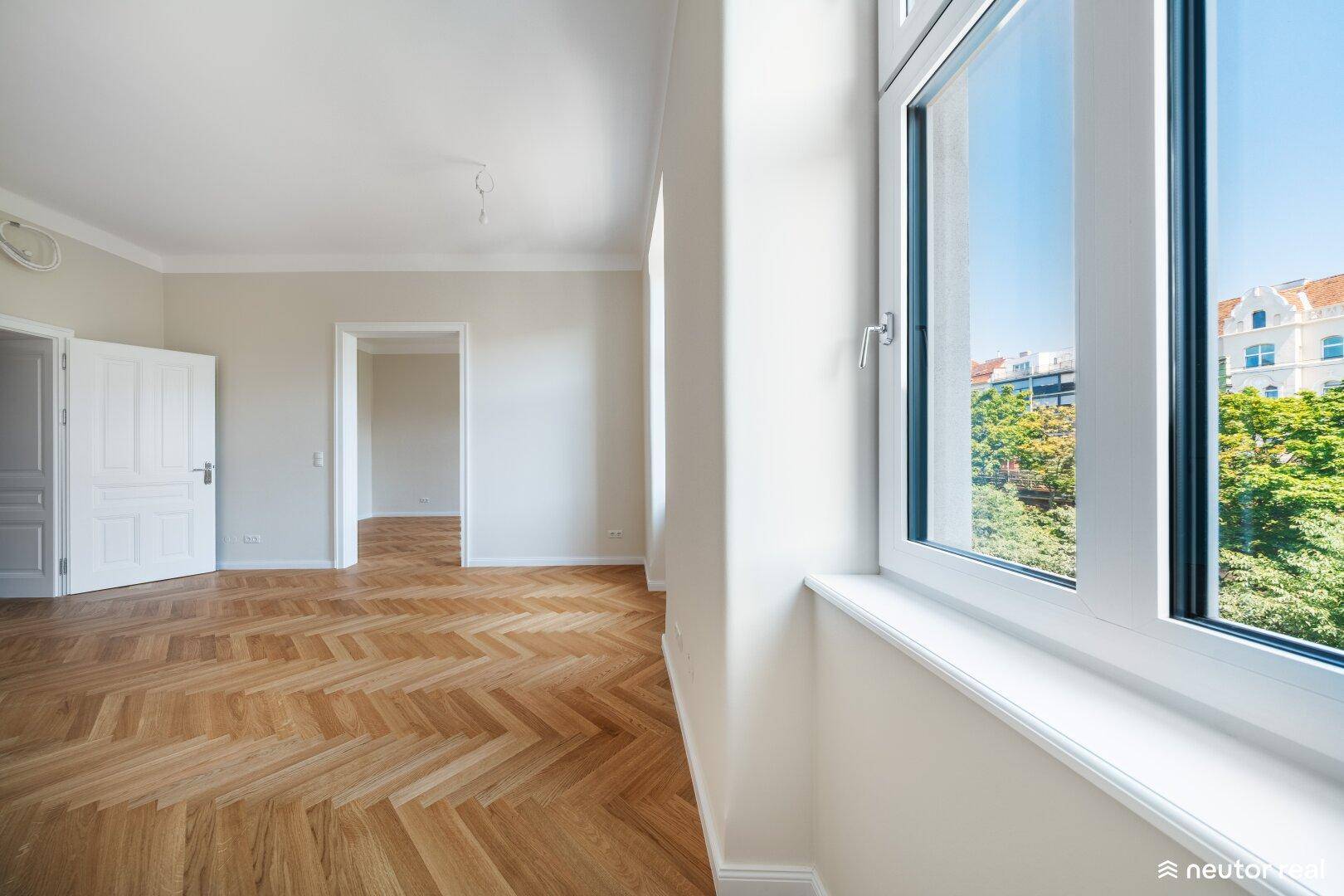Helles Wohnzimmer mit Fischgrätparkett und großen Fenstern, die einen Blick auf die Stadt ermöglichen.