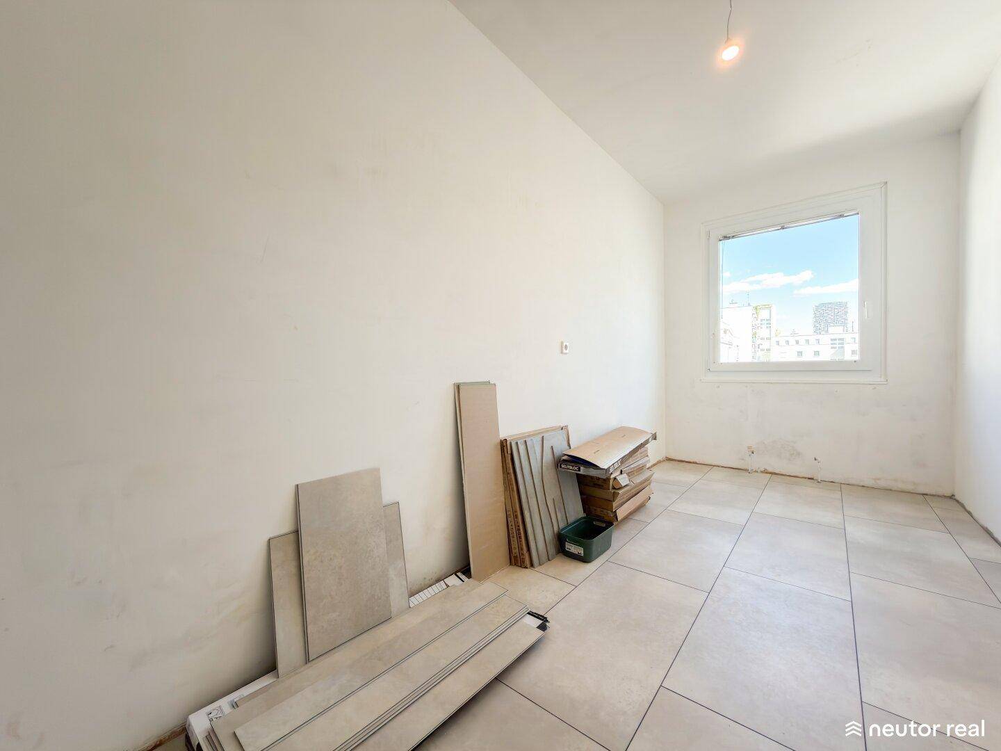 Leerer Raum mit Fliesenboden und Baumaterialien, bereit für die Renovierung.