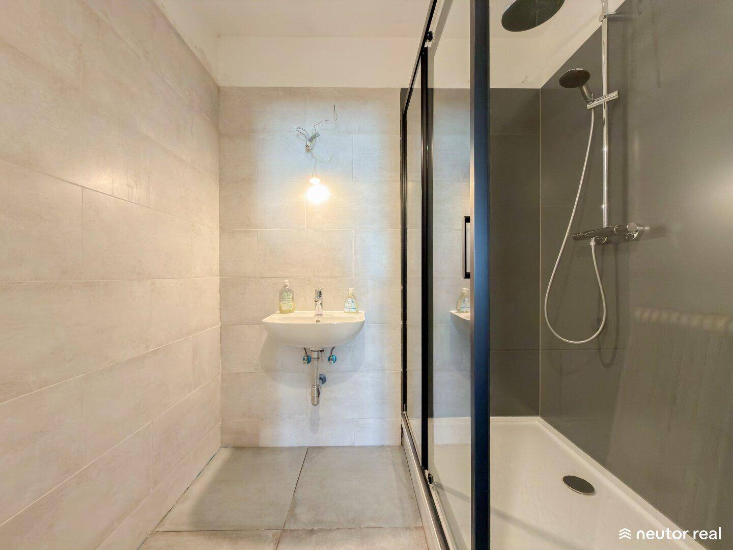 Badezimmer mit moderner Duschkabine, Einzelwaschbecken und hellen Fliesen.