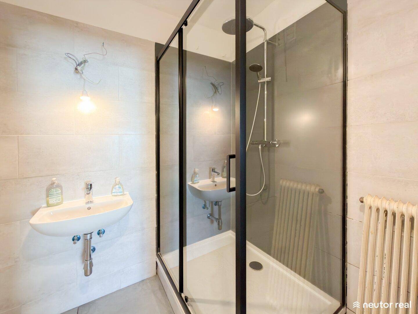 Badezimmer mit Duschkabine, zwei Waschbecken und Heizkörper an der Wand.