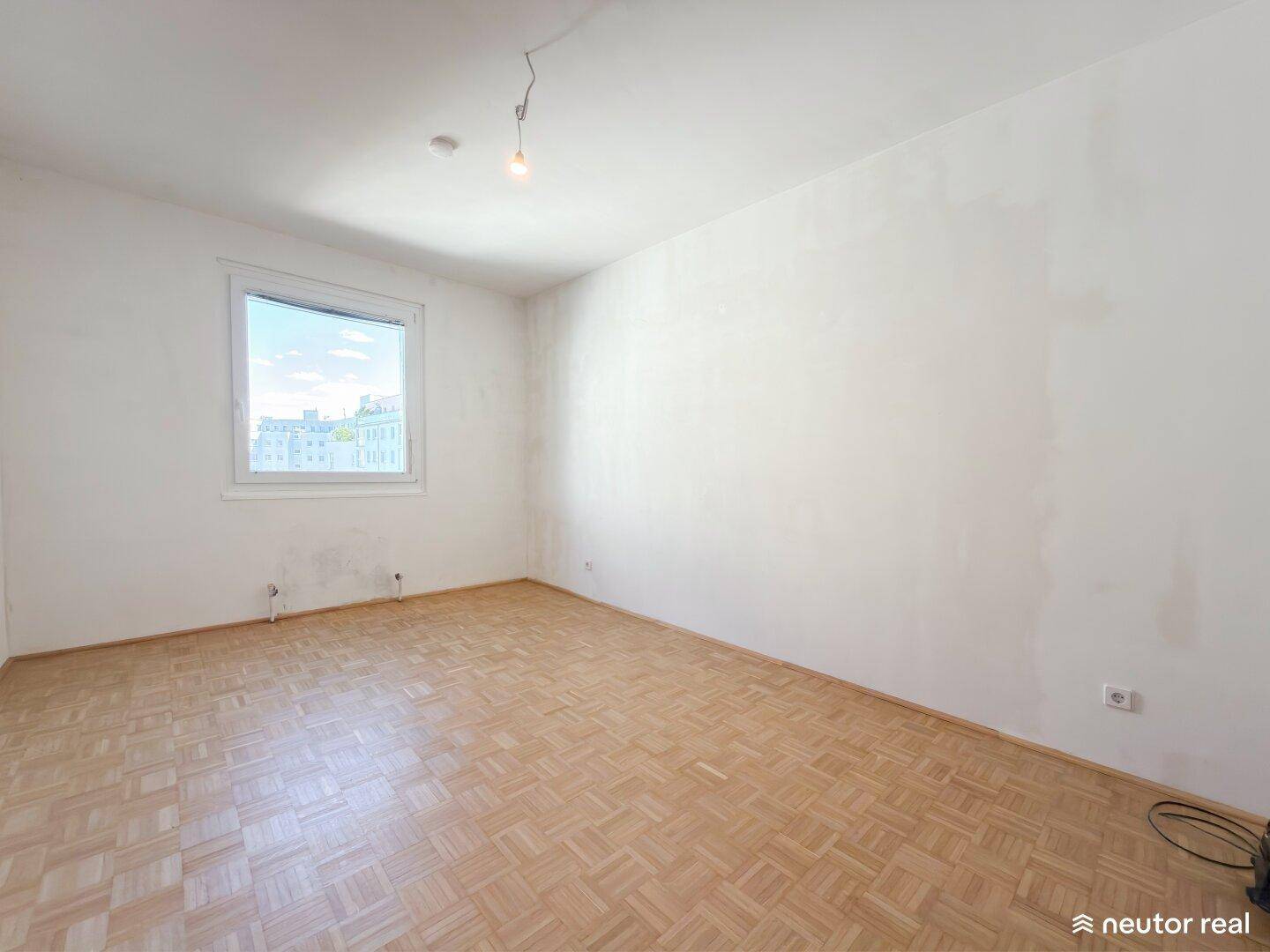 Geräumiges leeres Zimmer mit Fischgrätparkett und hellem Fenster.
