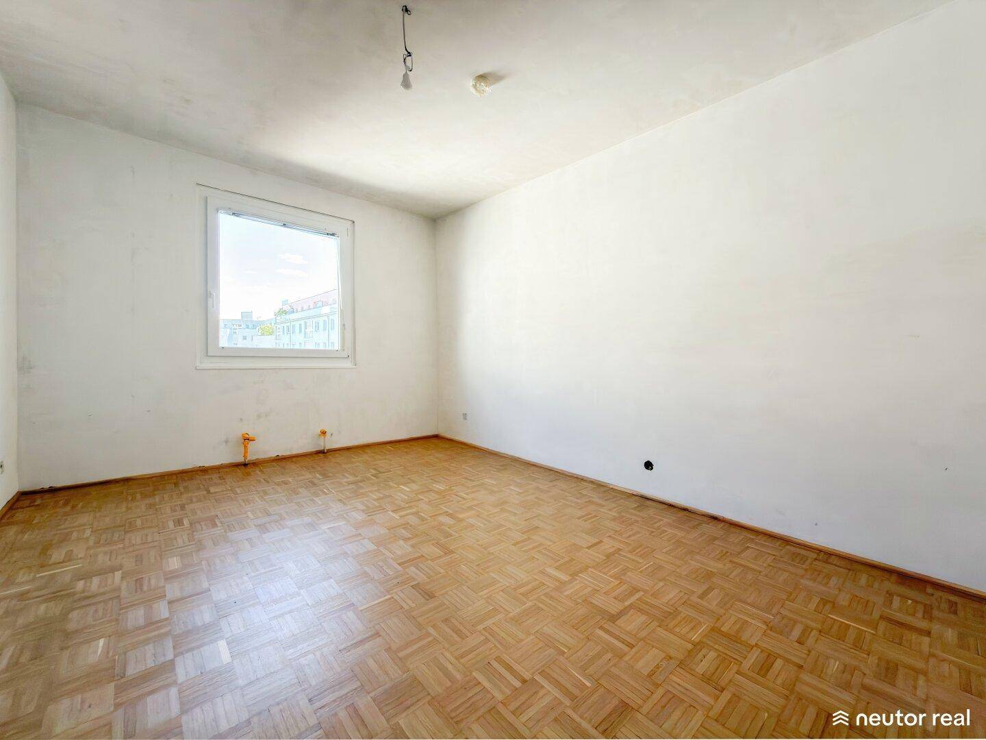 Leeres Zimmer mit Fischgrätparkett und Fenster, das auf die Stadt blickt.