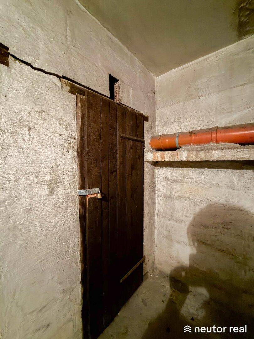 Rustikaler Kellerraum mit Holztür und unverputzten Wänden, ideal als Lagerfläche.
