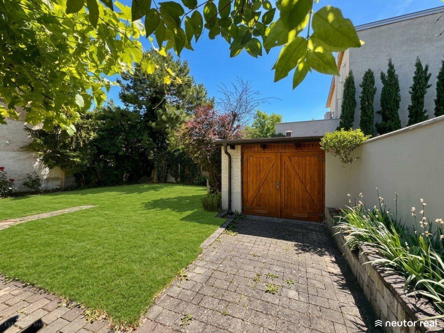 Grüner Garten mit Rasenfläche, gepflasterter Auffahrt und Holzgarage.