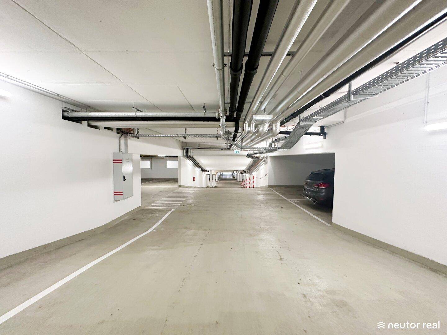 Lange Tiefgaragenzufahrt mit Betonboden, weißen Wänden und sichtbaren Deckeninstallationen.