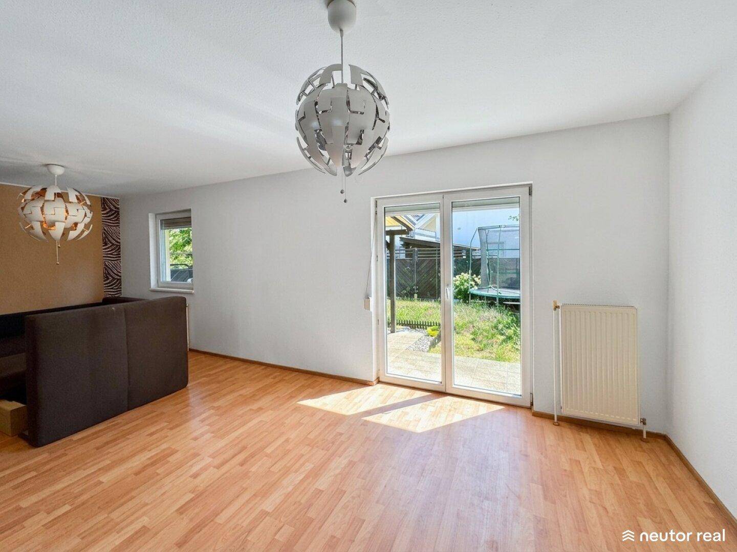 Geräumiges Wohnzimmer mit Laminatboden und großen Fenstertüren zum Außenbereich.