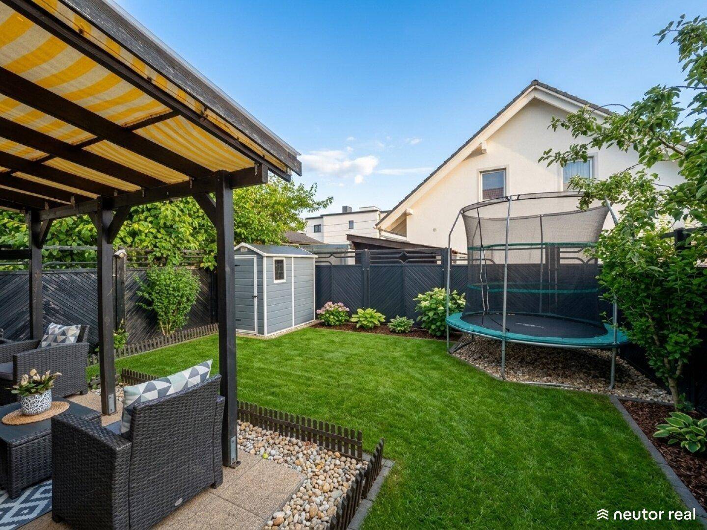 Gepflegter Garten mit Rasenfläche, Gartenhaus und Trampolin, ideal für Familien.