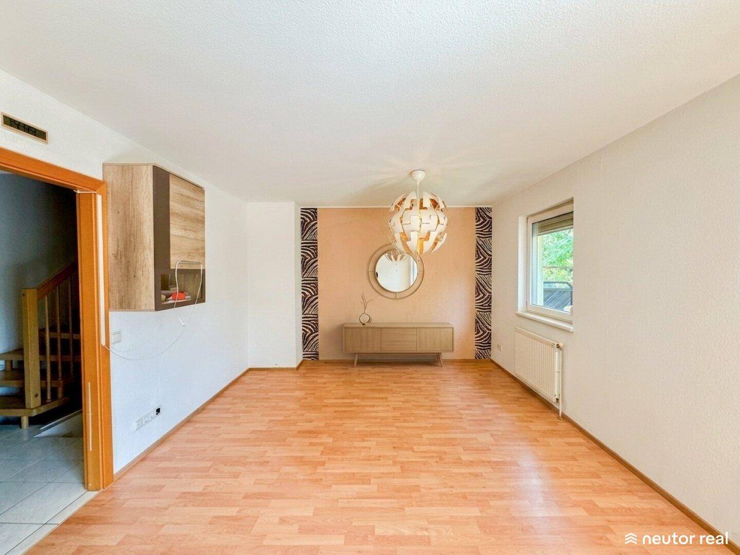 Heller Wohnbereich mit Laminatboden, dekorativer Wandgestaltung und Fenster.