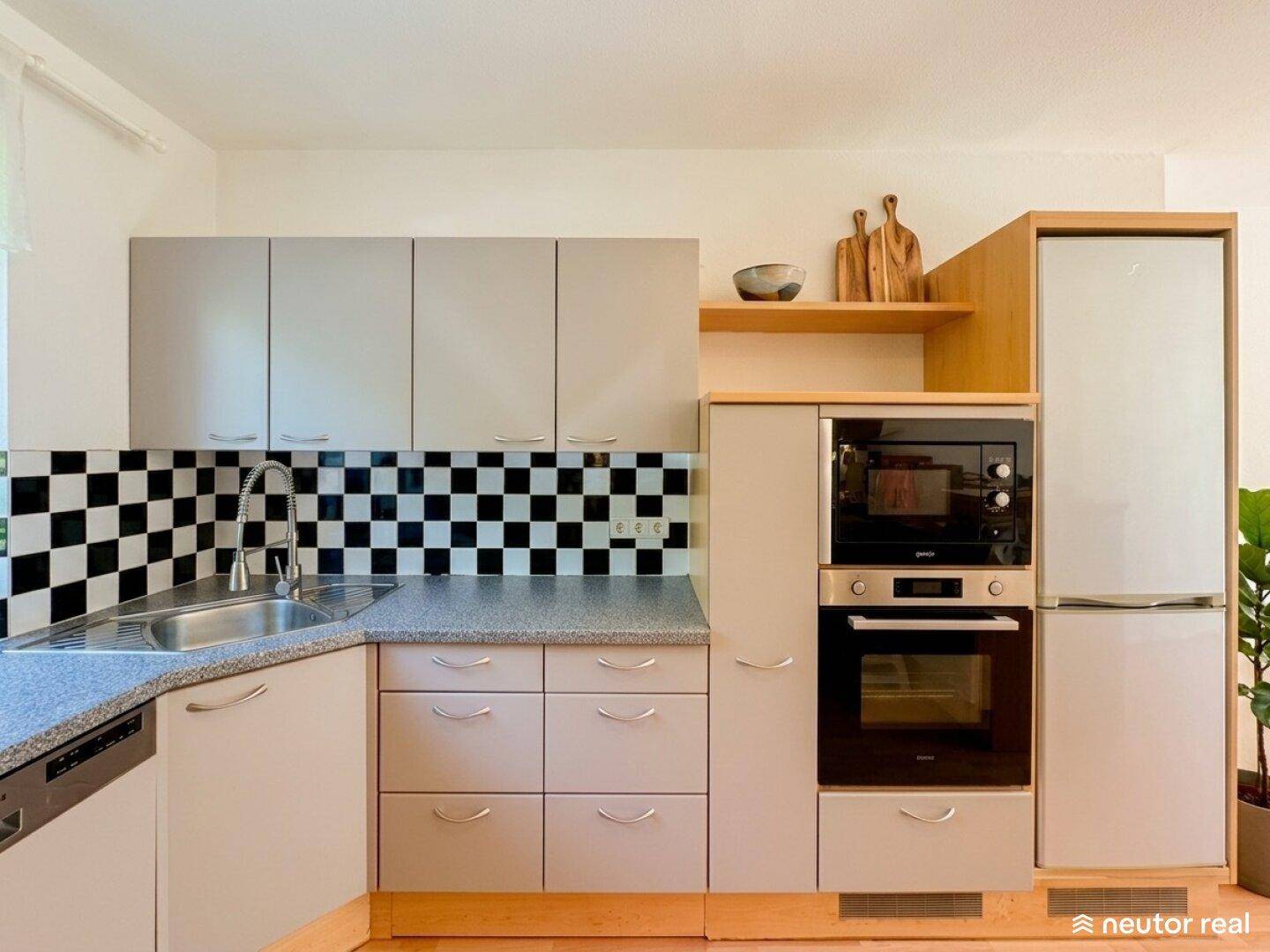 Detailansicht der Küche mit integriertem Backofen, Mikrowelle und Kühlschrank.