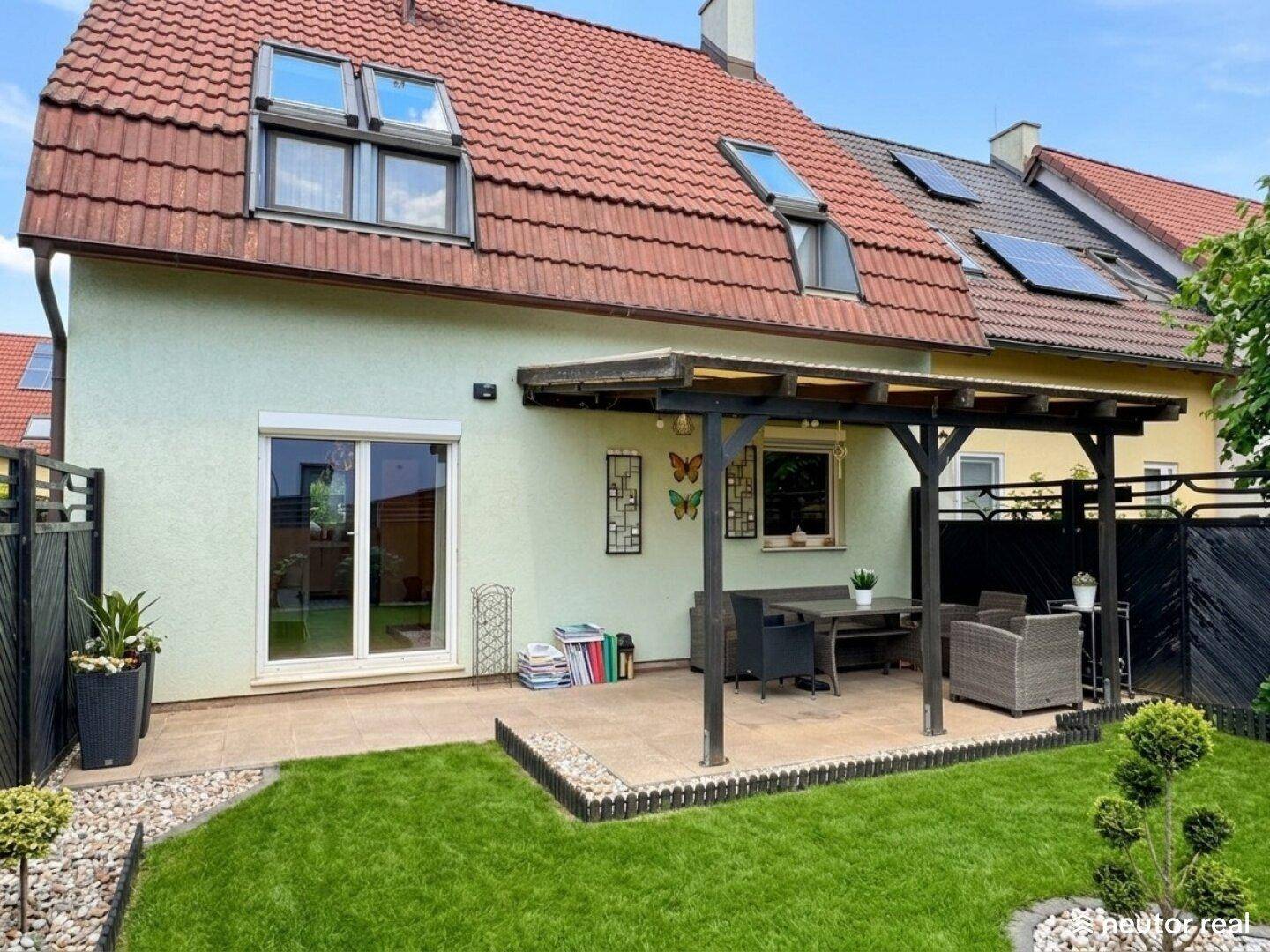 Sonnige Terrasse mit Überdachung und angrenzendem Rasenbereich, ideal für Mahlzeiten im Freien.