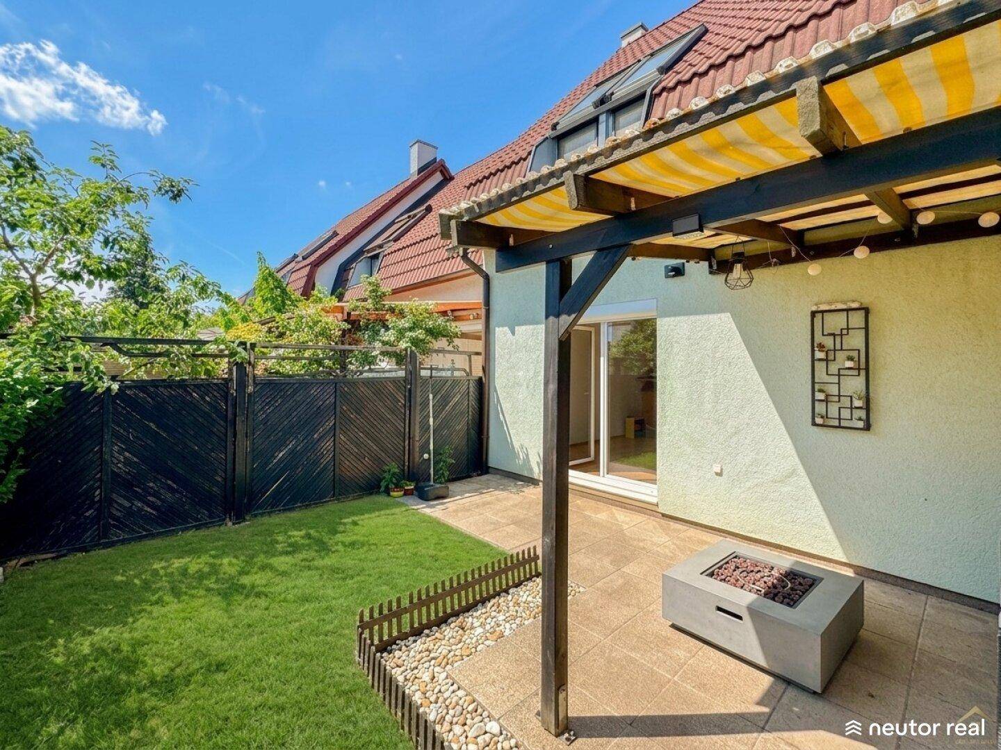 Gemütliche Terrasse mit Überdachung, Rasenfläche und moderner Feuerstelle für Abende im Freien.