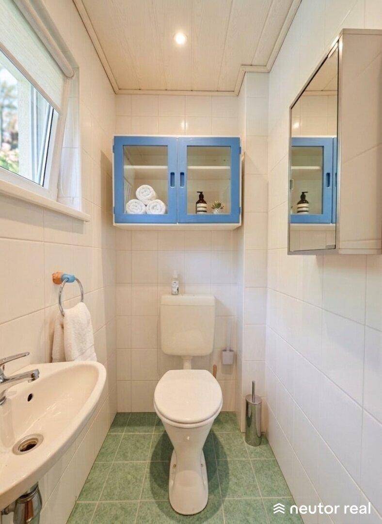 Kleines Gäste-WC mit Fenster, Waschbecken und blauen Bodenfliesen.