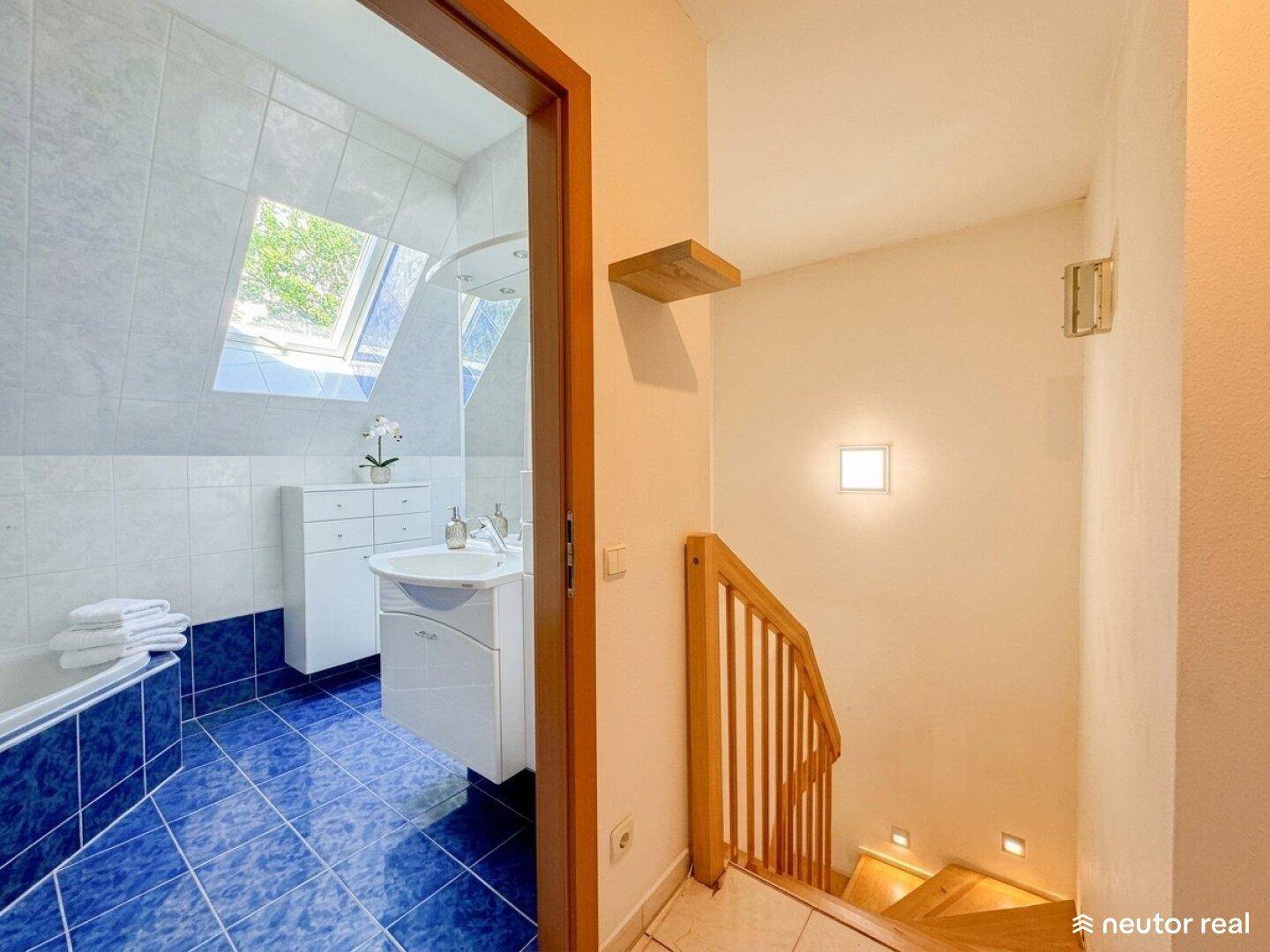Blick vom Flur in ein Badezimmer mit blauen Fliesen und Dachfenster.
