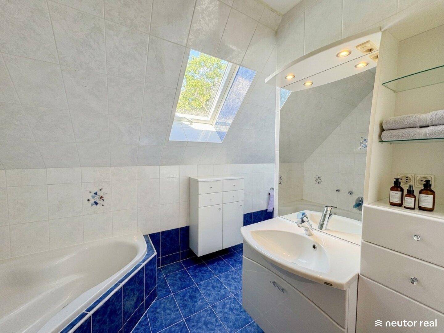 Badezimmer mit Badewanne, Waschbecken, großem Spiegel und natürlichem Licht durch Dachfenster.