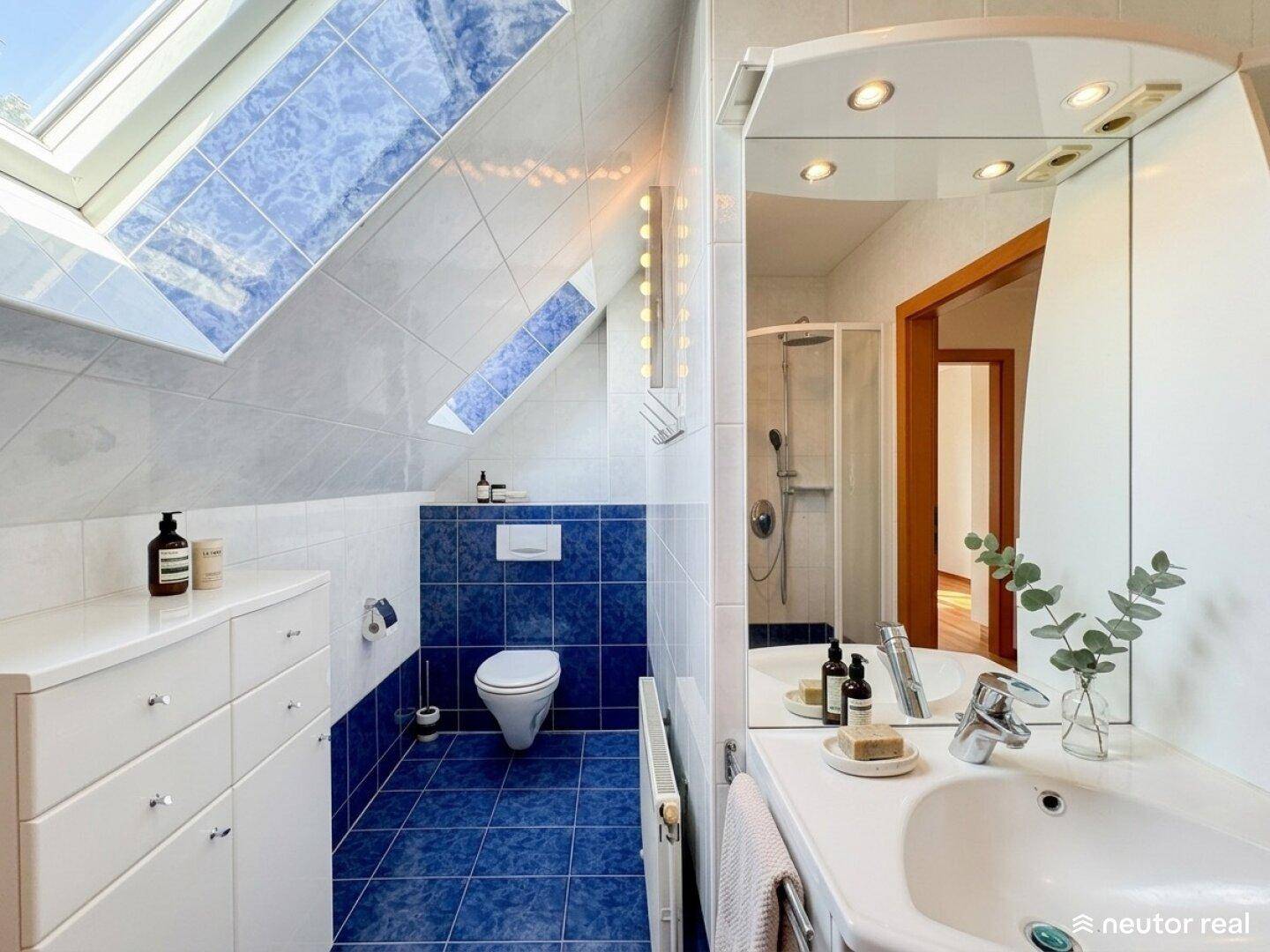 Modernes Badezimmer mit Dusche, WC, Waschbecken und viel Tageslicht durch Dachfenster.