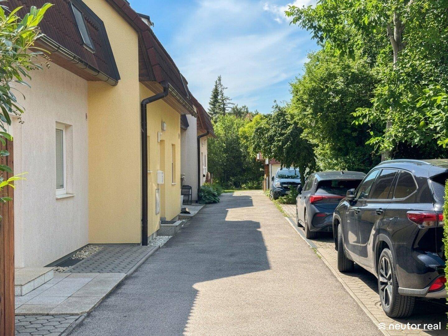 Ruhige Wohnstraße mit geparkten Autos und Reihenhäusern im Grünen.