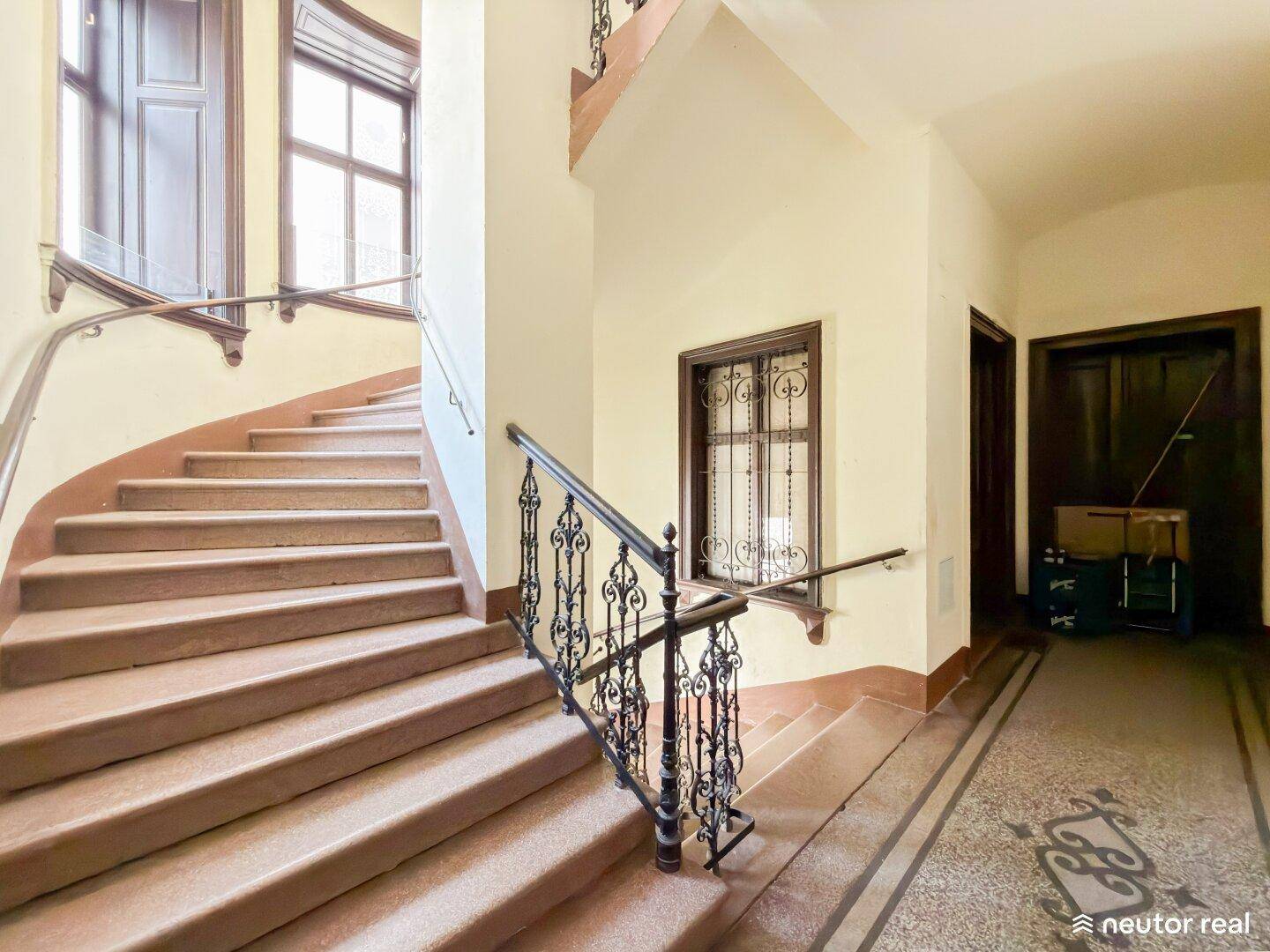 Historisches Treppenhaus mit kunstvollen Geländern und breiten Stufen in einem Altbau.