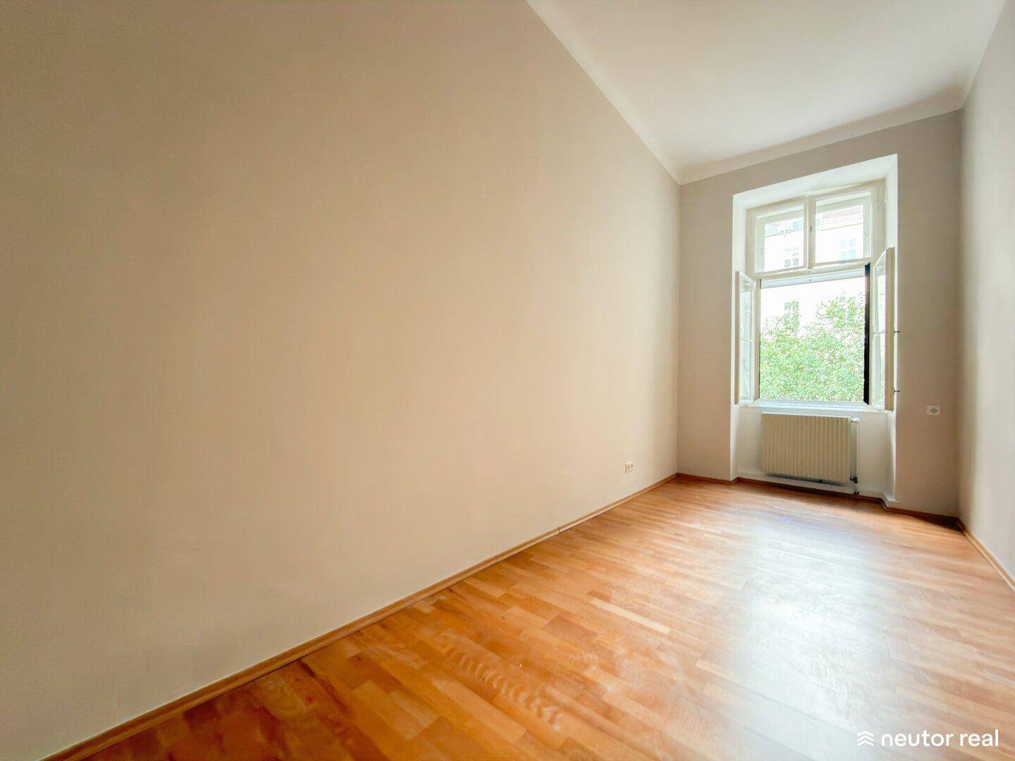 Leerer Raum mit Parkettboden und einem Fenster, das für natürliches Licht sorgt.