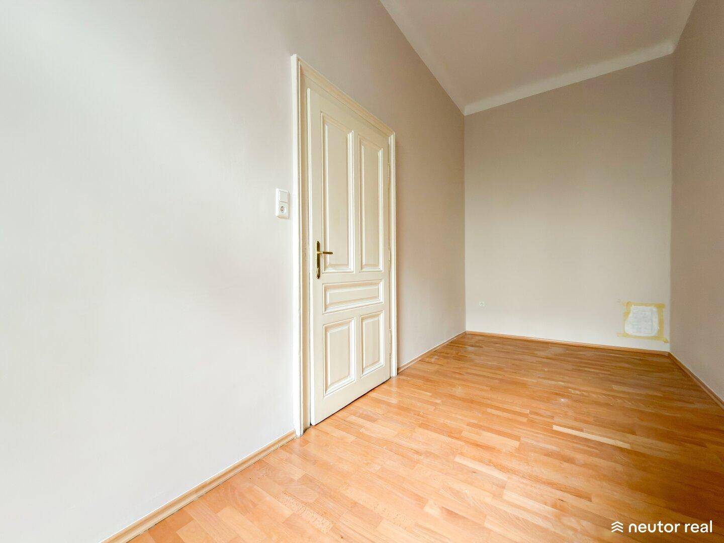 Leerer Raum mit Holzfußboden und einer Tür, der vielseitig genutzt werden kann.