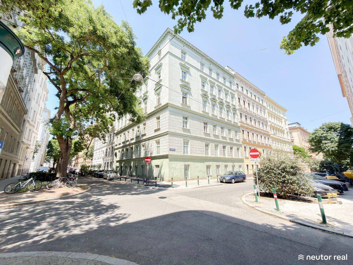 Historisches Eckgebäude an einer städtischen Straße mit vielen Fenstern und Bäumen.