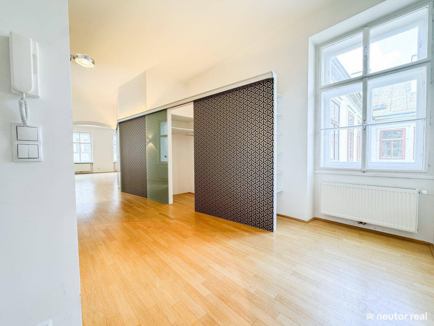 Langer Flur mit Holzboden, großen Fenstern und einer modernen Schiebetür zum Ankleidebereich.