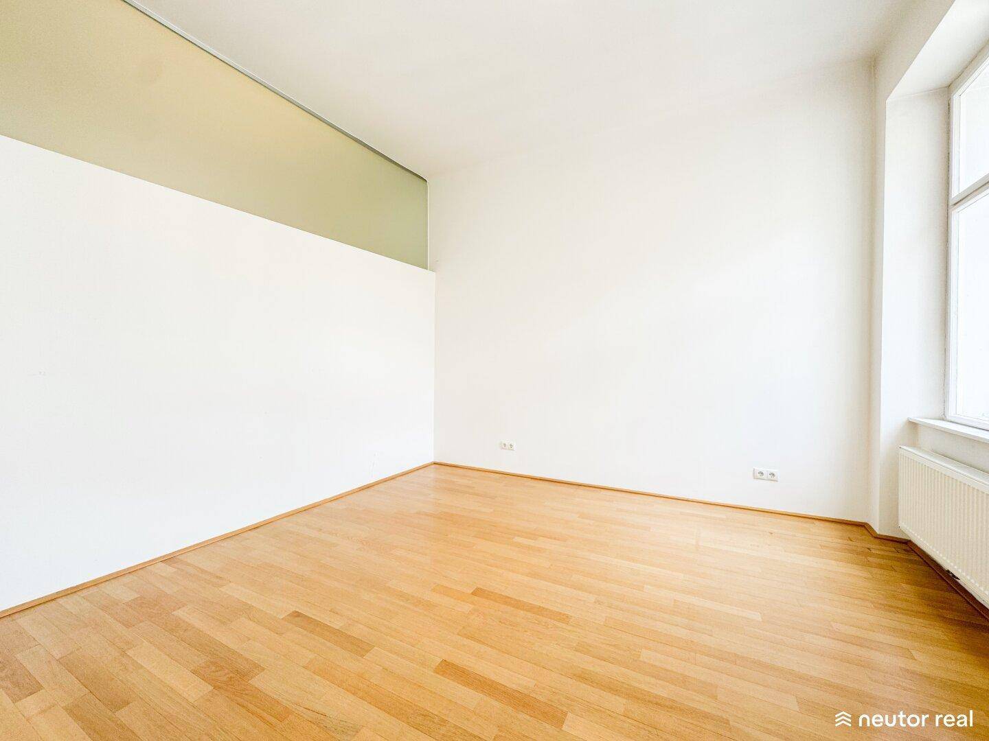 Helles Schlafzimmer mit Holzboden, weißen Wänden und einem großen Fenster für viel Tageslicht.