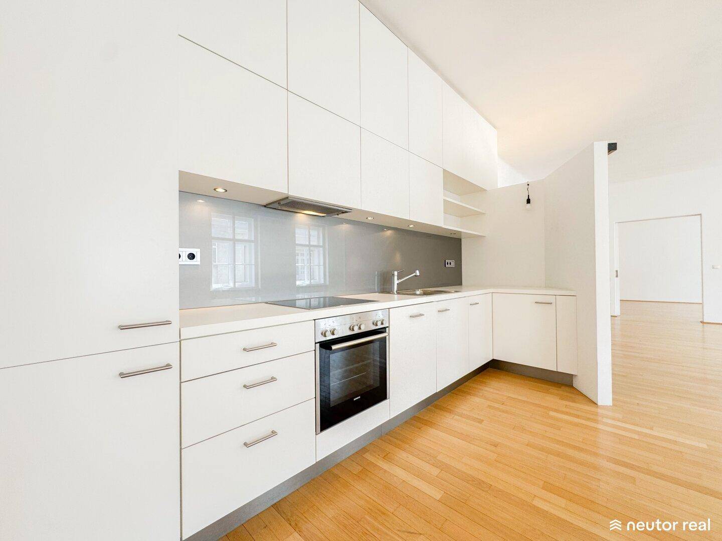 Moderne Einbauküche mit weißen Hochglanzfronten, integrierten Geräten und hellem Holzboden.