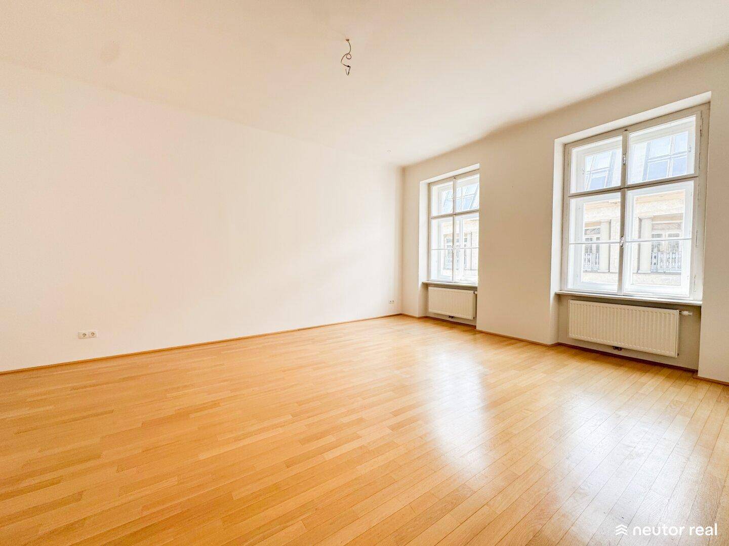Helles Wohnzimmer mit Holzboden und zwei großen Fenstern, die viel Tageslicht bieten.