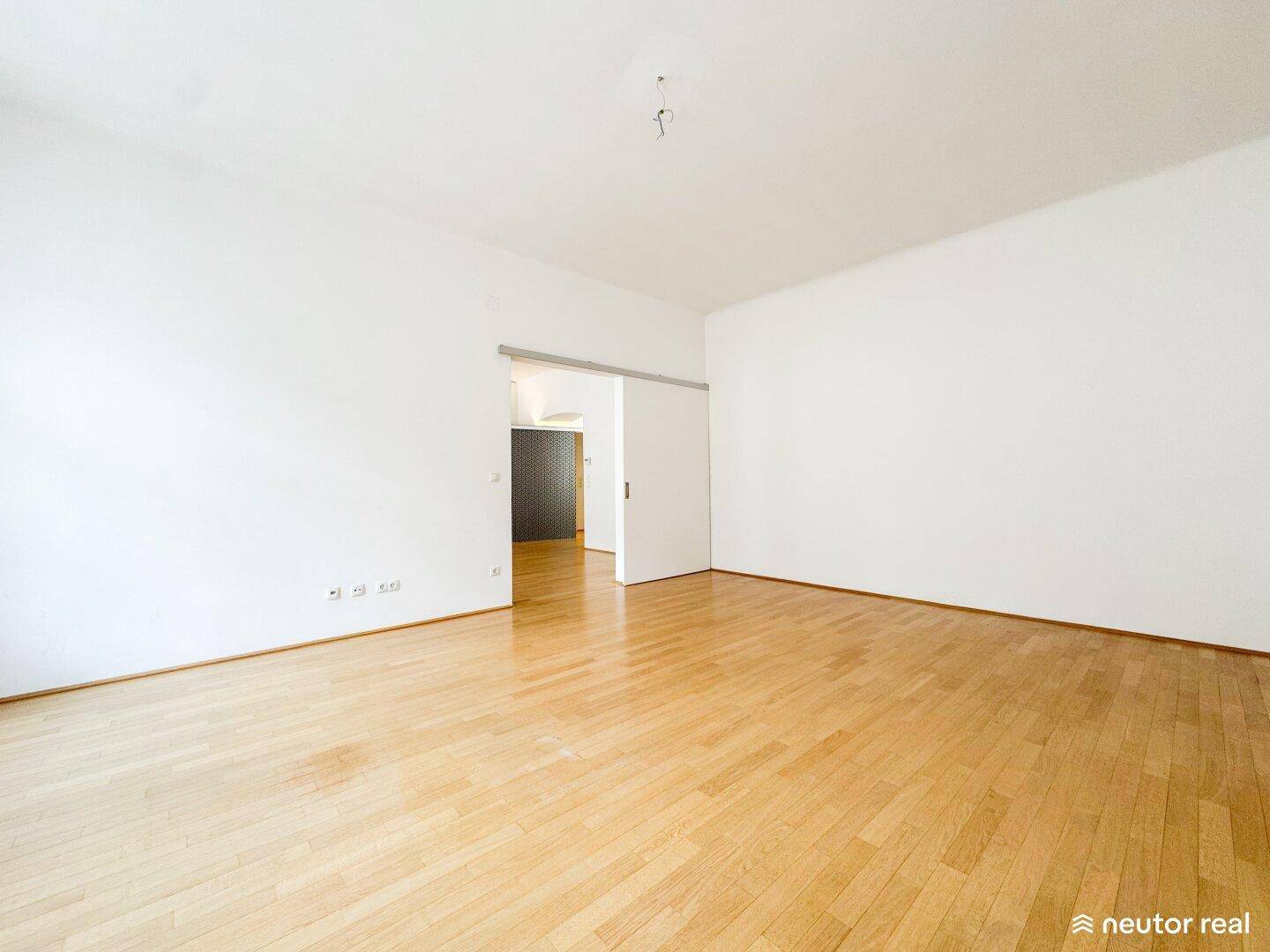 Geräumiges Wohnzimmer mit Holzboden und einer Schiebetür, die den Raum flexibel gestaltet.