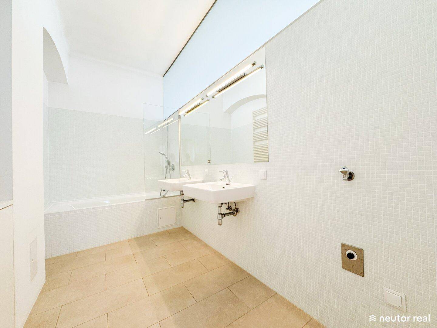 Modernes Badezimmer mit zwei Waschbecken, Badewanne und hellen Fliesen.