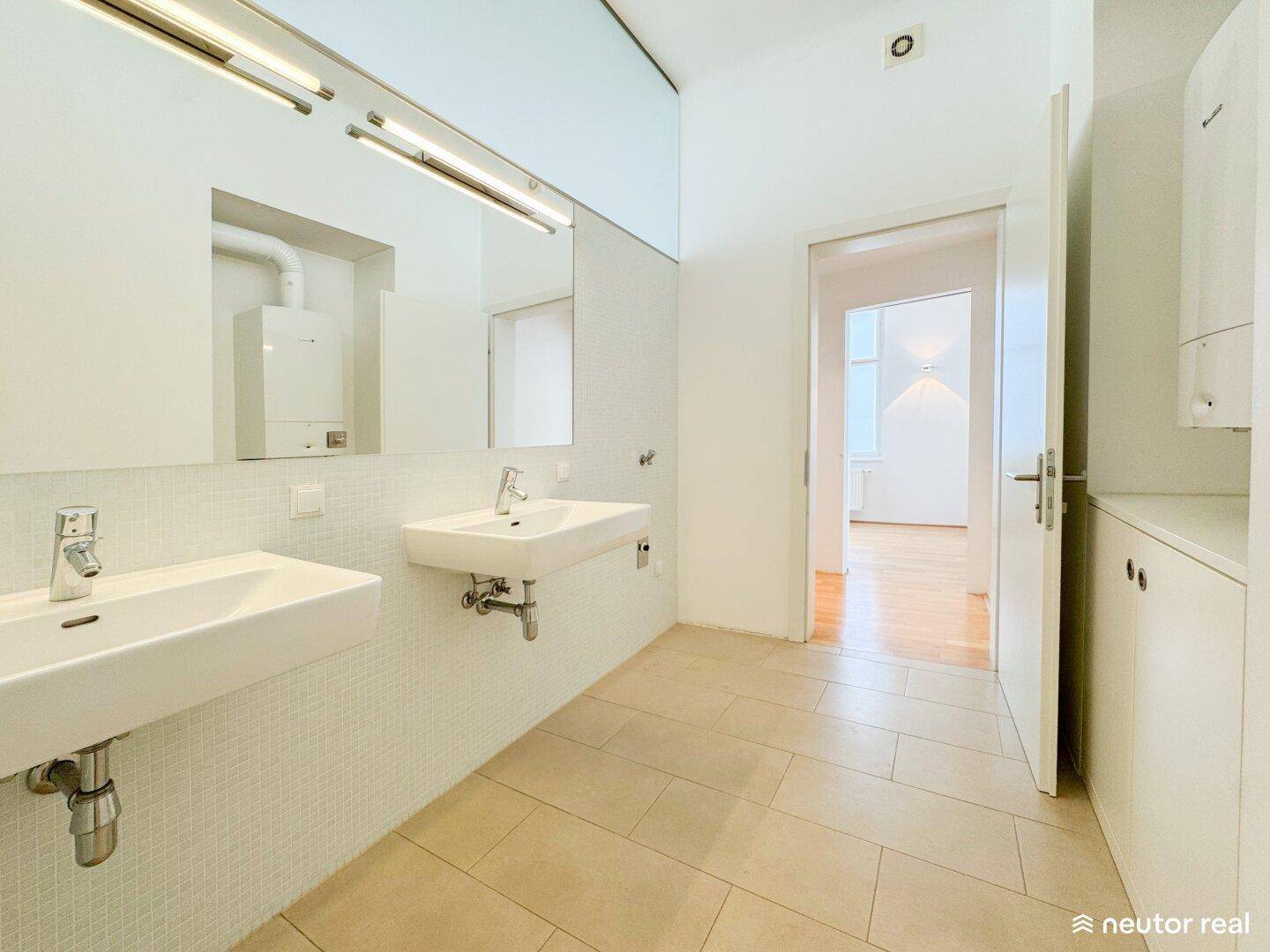 Helles Badezimmer mit Doppelwaschbecken, großem Spiegel und integriertem Warmwasserbereiter.