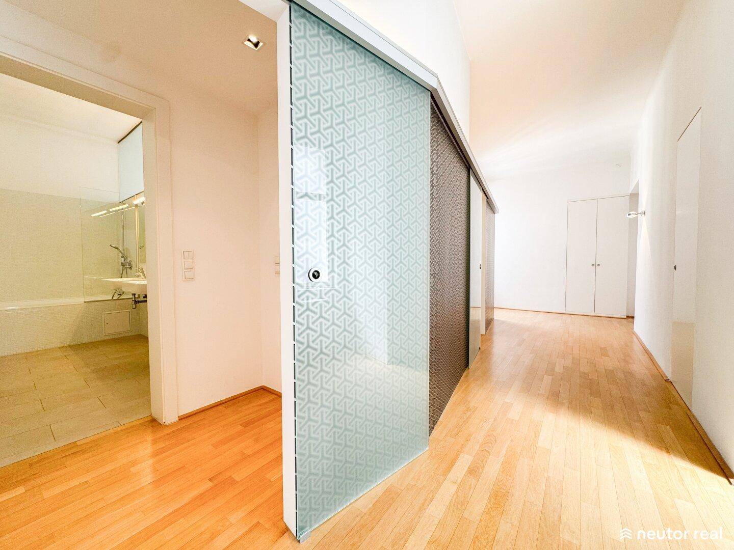 Heller Flur mit Holzboden, der zu einem Badezimmer und weiteren Räumen führt.