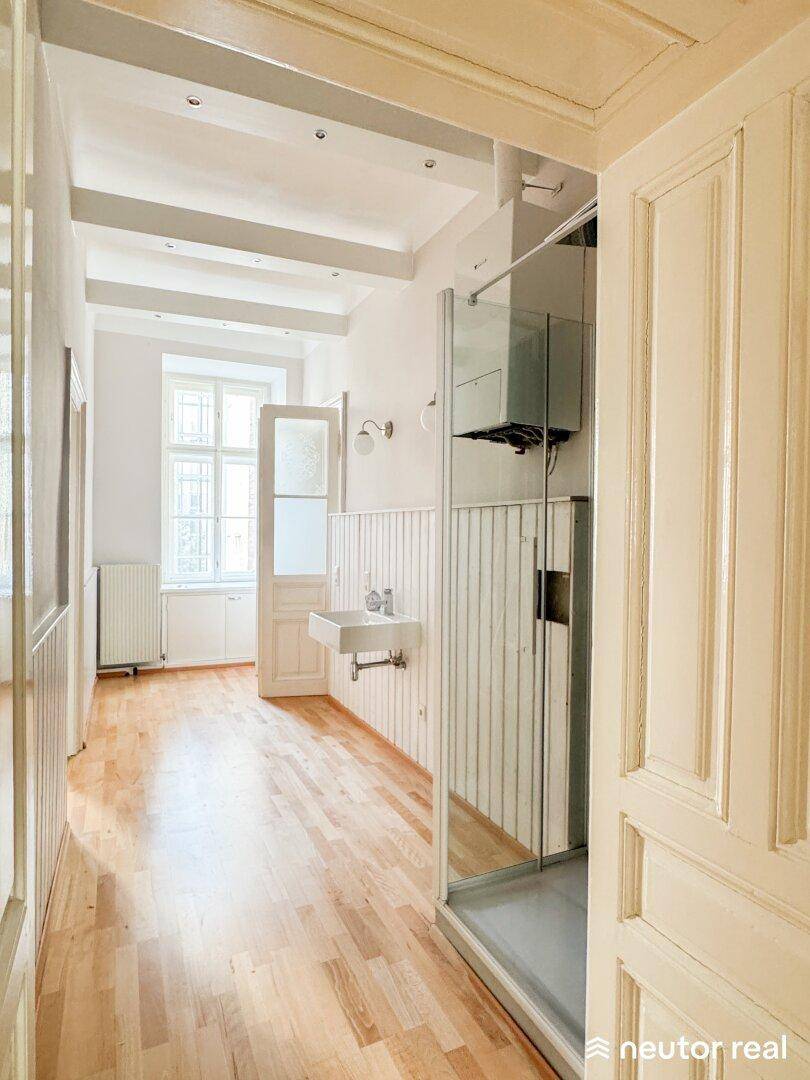 Langer Raum mit Holzboden, Fenster und einer Duschkabine sowie einem Waschbecken.