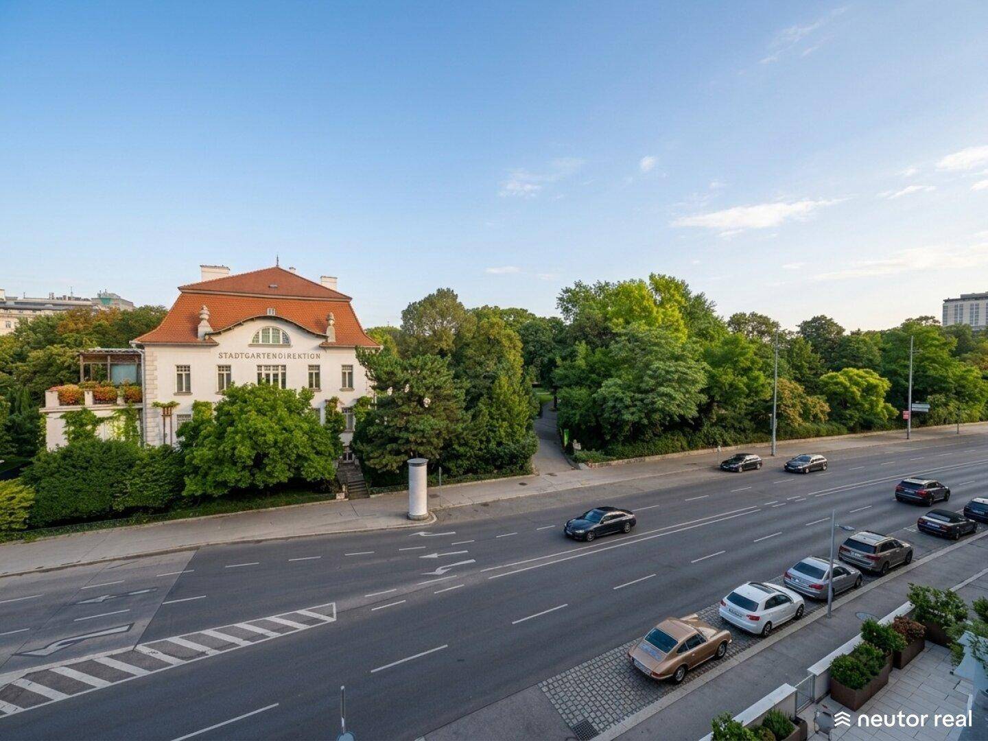 Weitläufige Stadtansicht mit einer belebten Straße, einem historischen Gebäude und üppigem Grün.