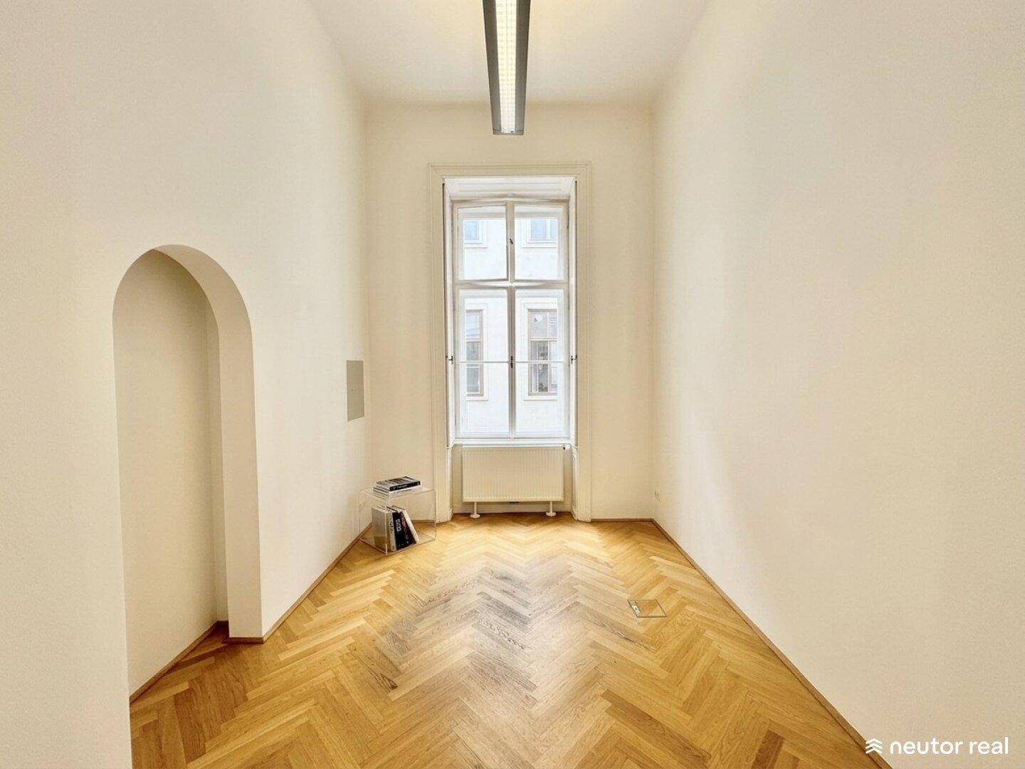 Leerer, heller Raum mit Fischgrätparkett, einem hohen Fenster und einer Nische.