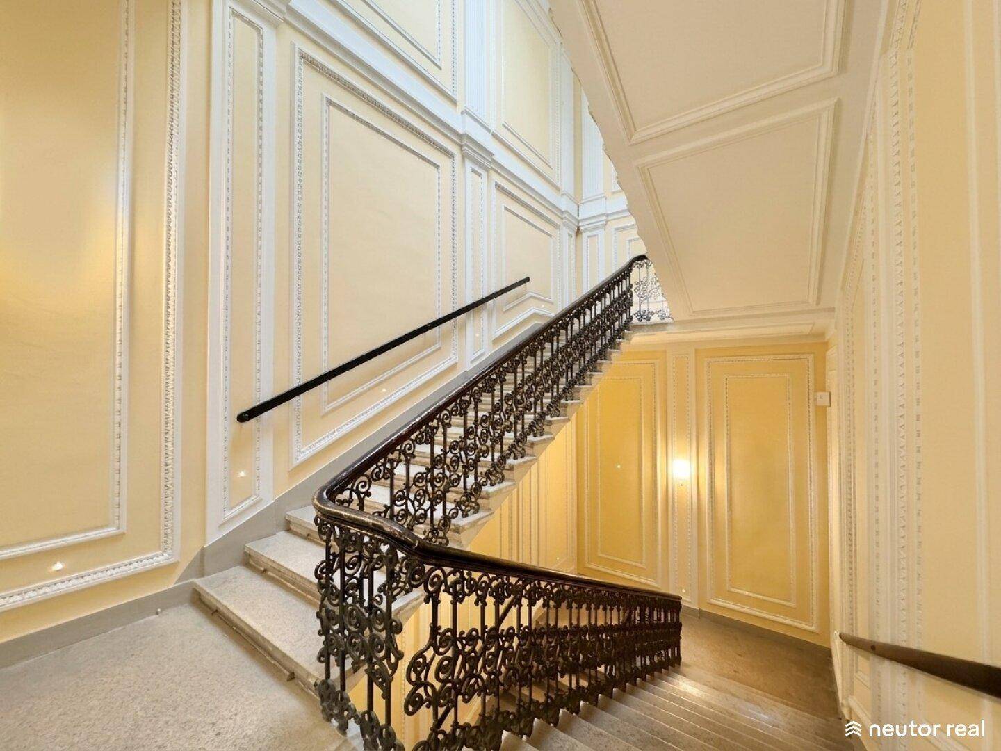 Elegantes Treppenhaus mit schmiedeeisernem Geländer, Stuckverzierungen und gelben Wänden.