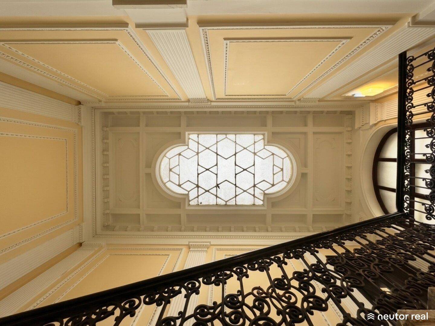 Blick nach oben in ein historisches Treppenhaus mit kunstvoller Decke und Oberlicht.