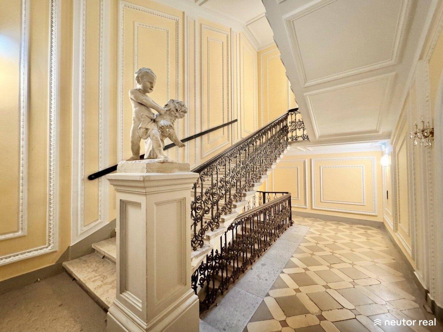 Eindrucksvolles Treppenhaus mit kunstvollem Geländer, klassischer Wandvertäfelung und einer Statue im Eingangsbereich.