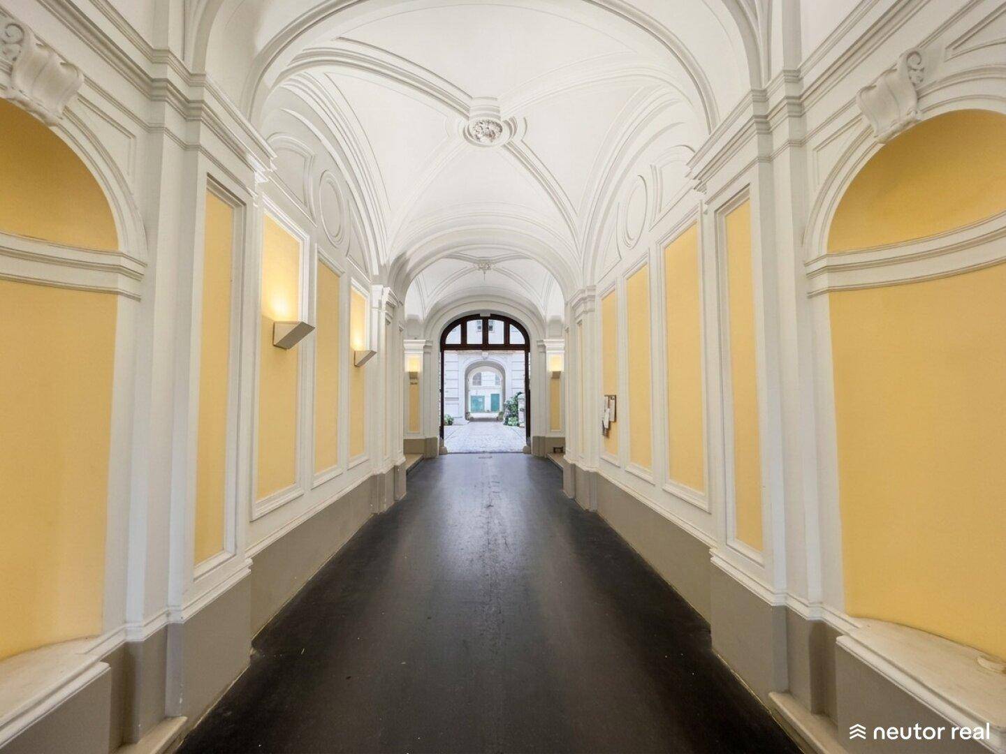 Langer, eleganter Flur mit gewölbter Decke, Wandvertäfelungen und einem Blick in den hellen Innenhof.