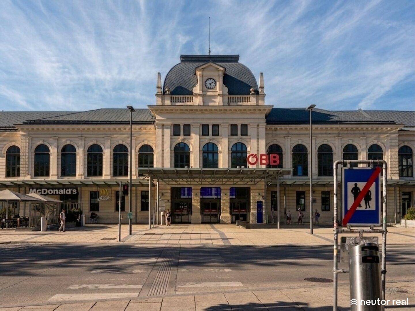 Historisches Bahnhofsgebäude mit Uhr, Rundbogenfenstern und klassischer Architektur.